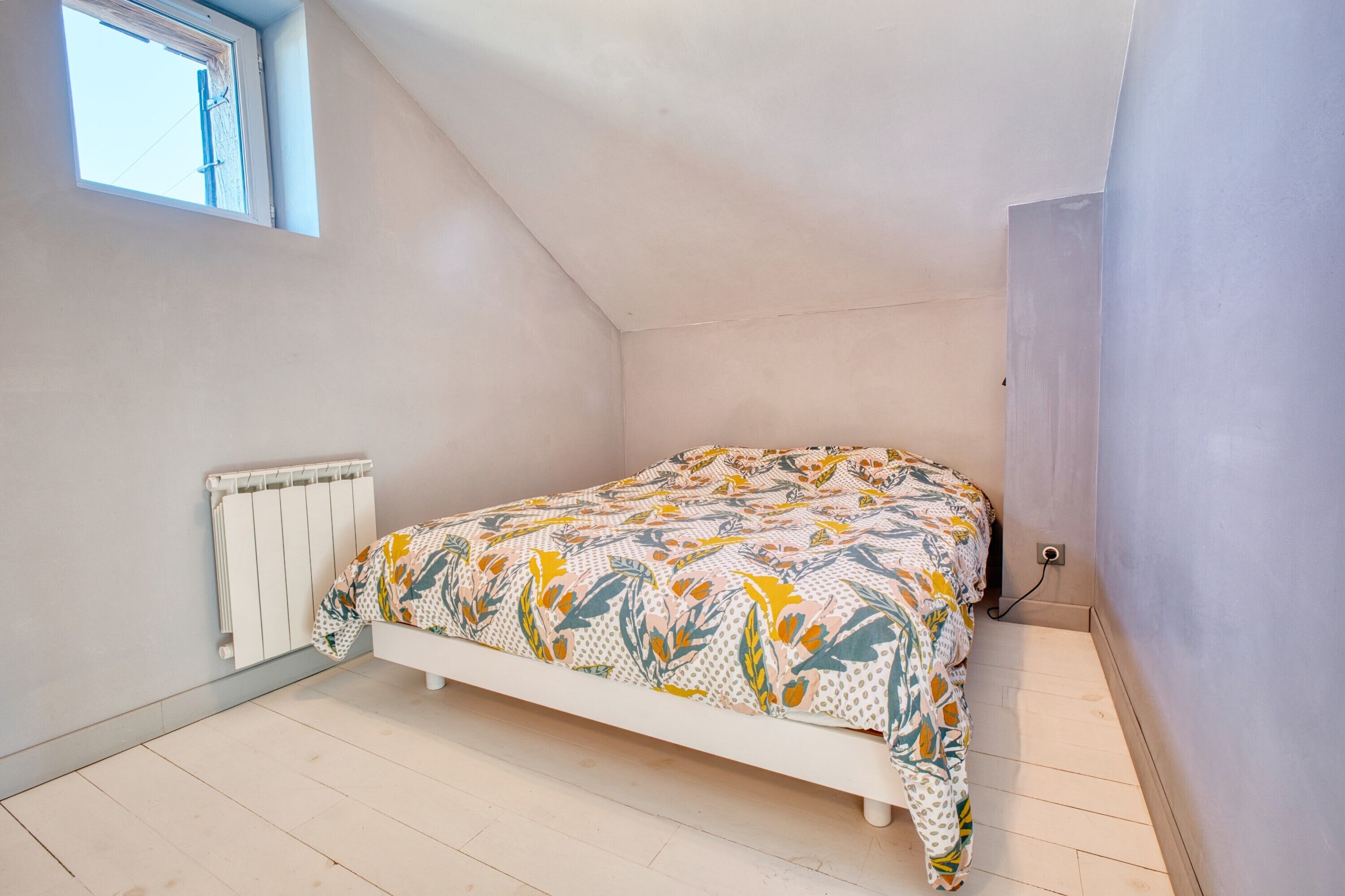 A small, single-bed room with a sloped ceiling, a radiator, and a window.