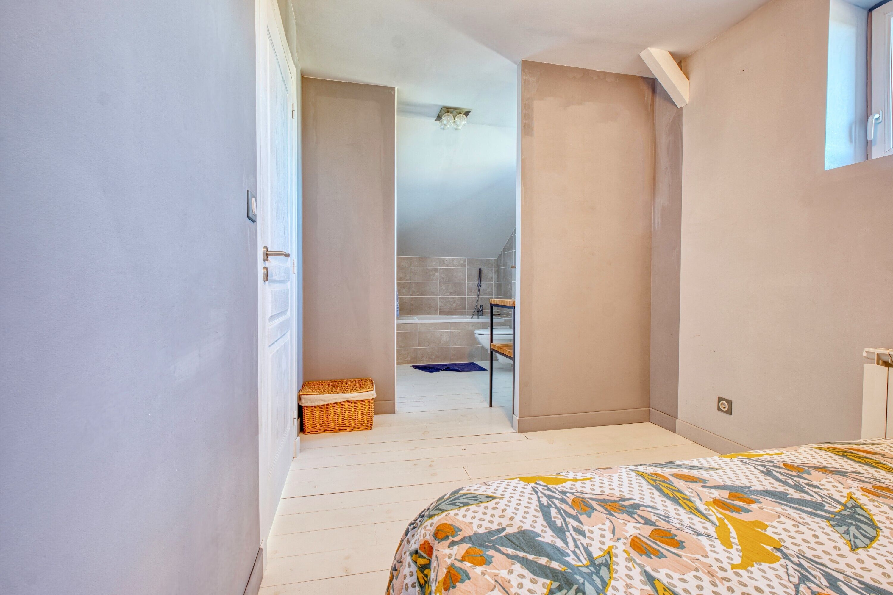 A bedroom with a bed, a door leading to a bathroom, and a small wicker basket.