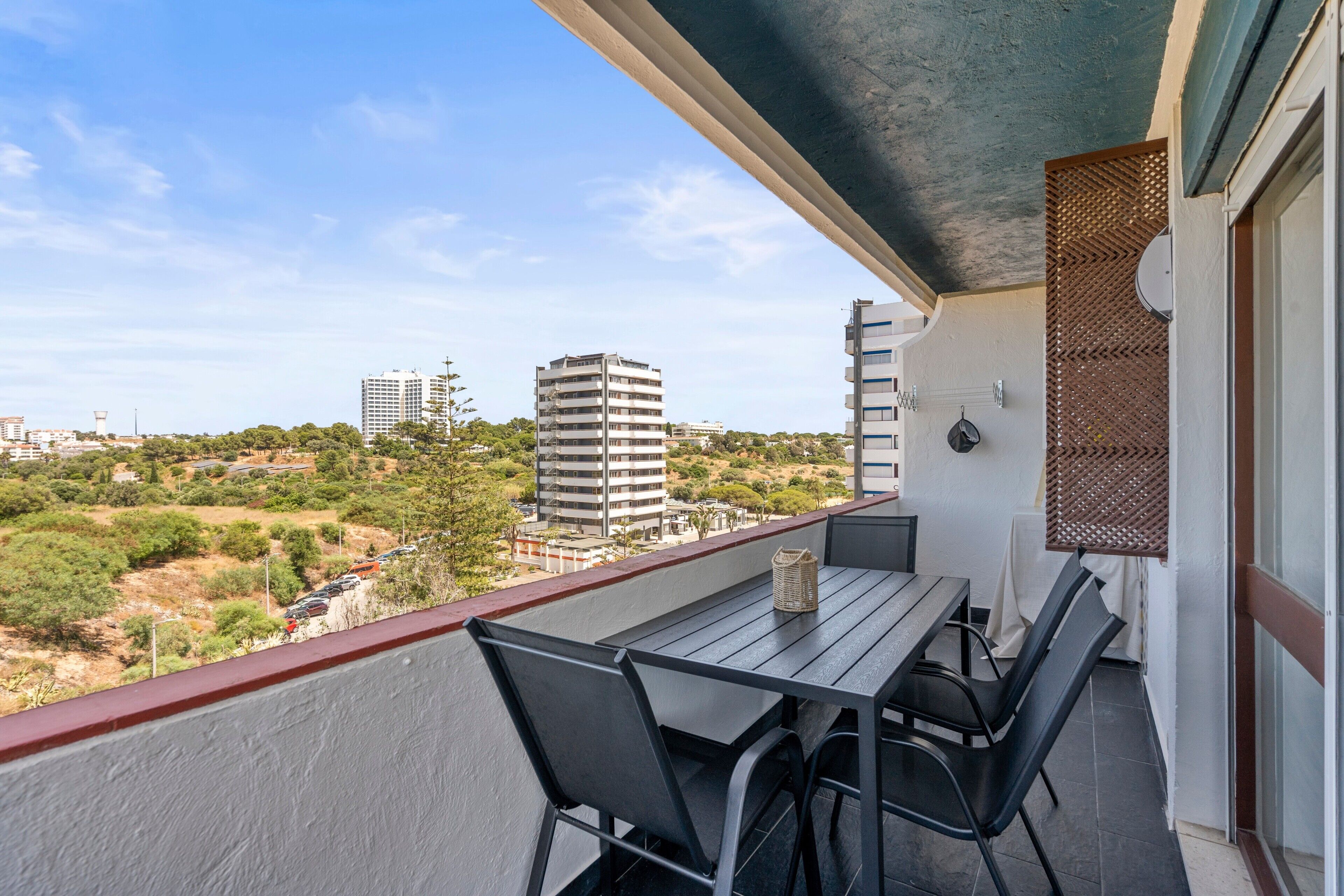 A balcony with a table and chairs, overlooking a cityscape with buildings and greenery.