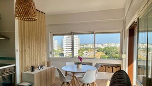 A modern kitchen with a built-in oven, a dining area with a round table and chairs, and a large window with a city view. - Apartment 'Sunset' with Sea View, Wi-Fi and Air Conditioning (Alvor)