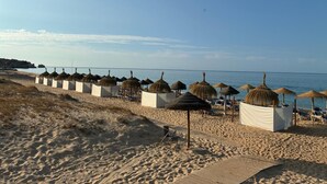 A beach with rows of thatched umbrellas and lounge chairs, a wooden boardwalk, and a clear view of the sea. - Apartment 'Sunset' with Sea View, Wi-Fi and Air Conditioning (Alvor)