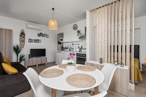 Un salon moderne avec une table à manger blanche, un canapé et une cuisine en arrière-plan.
