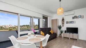 A modern living room with a balcony, a sofa, a TV, and a view of the city. - Apartment 'Sunset' with Sea View, Wi-Fi and Air Conditioning (Alvor)