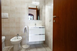 A bathroom with a bidet, a sink, a mirror, and a wooden door.