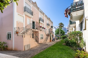 A narrow street with multi-story buildings, a paved walkway, and potted plants.
