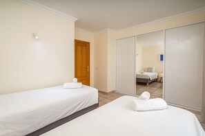 Quarto de hotel com duas camas, um guarda-roupa e um espelho refletindo outro quarto.