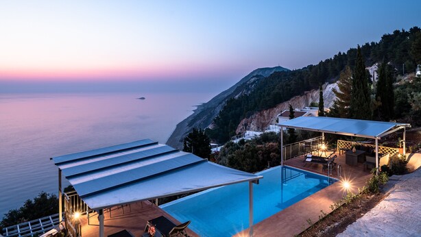 Ein Pool mit überdachtem Bereich, Gartenmöbeln und Blick auf das Meer im Abenddämmerung.