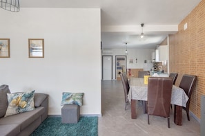 A modern living room with a sofa, a small table, and a dining area with chairs.