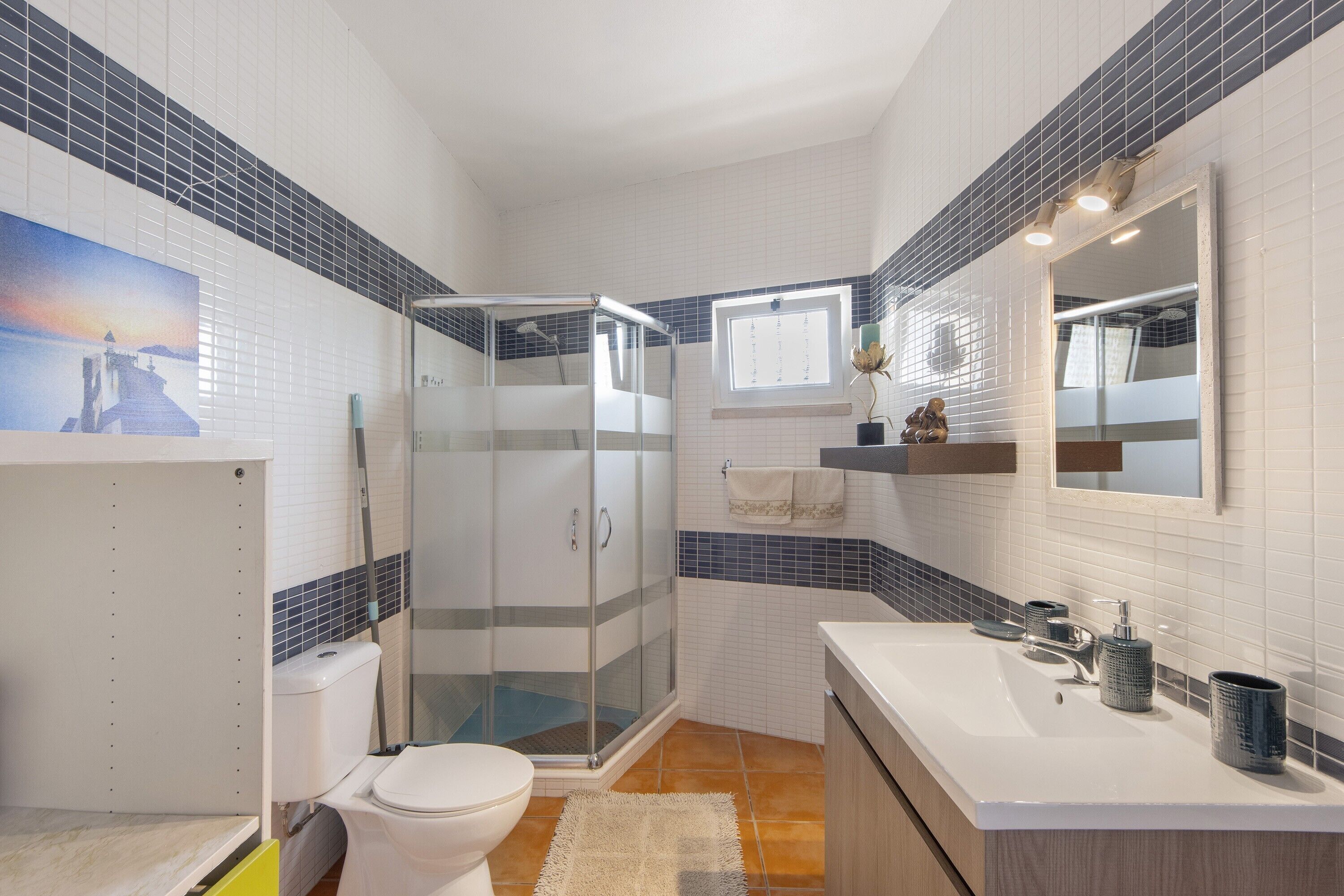Een badkamer met een douchecabine, een wit toilet, een wastafel met spiegel en een raam.