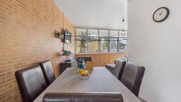 A dining area with a brick wall, a table with a patterned tablecloth, and a clock on the wall.