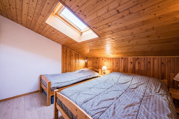 A room with two wooden beds, a skylight, and a small table with a lamp.