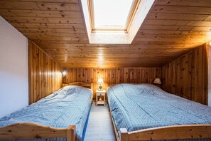 Una habitación con dos camas, un tragaluz, paredes de madera y una mesita de noche con lámpara.
