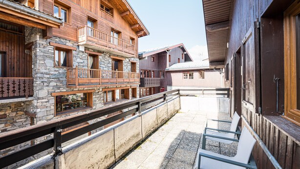 A wooden building with balconies and stone walls, a covered outdoor seating area, and a clear sky.