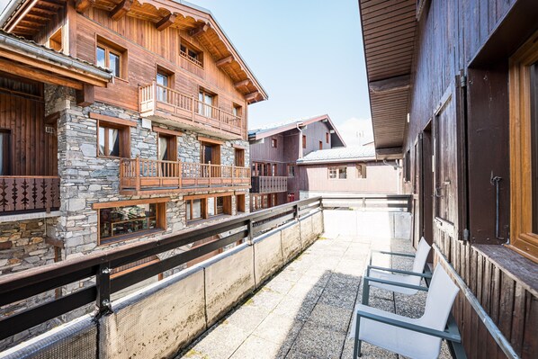 A wooden building with balconies and stone walls, a covered outdoor seating area, and a clear sky.