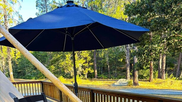 A deck with a fire pit, a blue umbrella, and a wooden chair. - This tipi is a 0 bedroom(s), 1 bathrooms, located in O'Brien, OR. (O'Brien)