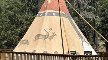 Ein Tipi mit einer Holzplattform und Bänken, umgeben von einem Holzzaun.
