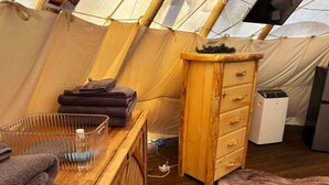 A cozy tent interior with a wooden desk, a drawer unit, a heater, and a bed with a fur throw. - This tipi is a 0 bedroom(s), 1 bathrooms, located in O'Brien, OR. (O'Brien)