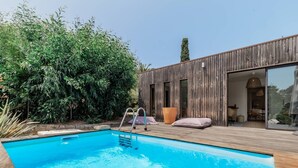 A swimming pool with a wooden deck, surrounded by dense foliage and a modern wooden building with large windows. - Villa Punta – 2/3 Bedrooms, Pool, Domaine de la Pointe (Grosseto-Prugna)