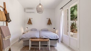 A bedroom with a bed, bedside tables, a hanging light fixture, and a view of greenery through a sliding door. - Villa Punta – 2/3 Bedrooms, Pool, Domaine de la Pointe (Grosseto-Prugna)