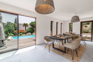 A modern dining area with a large table, wicker chairs, and a view of a swimming pool and garden.