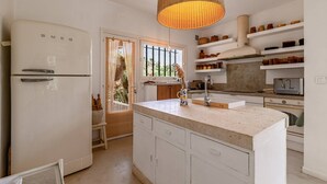 A modern kitchen with white cabinetry, a large island with a sink, and a hanging light fixture. - Villa Punta – 2/3 Bedrooms, Pool, Domaine de la Pointe (Grosseto-Prugna)