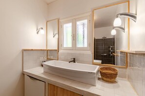 Ein modernes Badezimmer mit einem großen weißen Waschbecken, zwei Wandspiegeln und einer Duschkabine hinter einer Milchglasschiebetür.