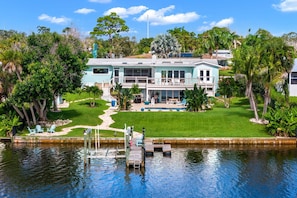 A two-story house with a swimming pool, dock, and lush greenery. - Mango Shores: Trendy Riverfront House w/Game Room, Speakeasy & Pool! (Melbourne)