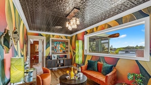 Een levendige woonkamer met een groot raam, een open haard en een kleurrijke abstracte muurschildering.