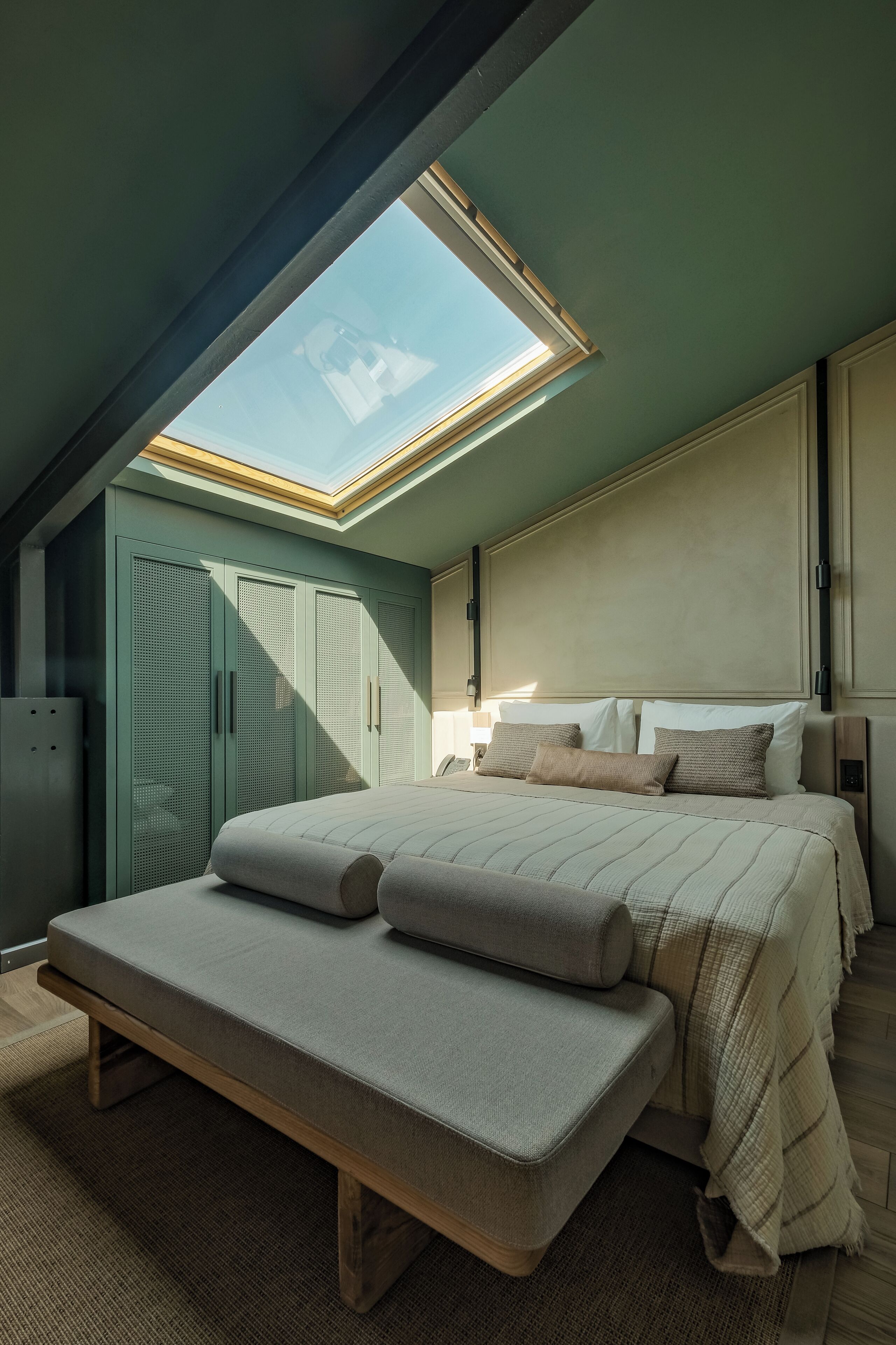 A bedroom with a skylight, a bed with a bench, and a wardrobe.