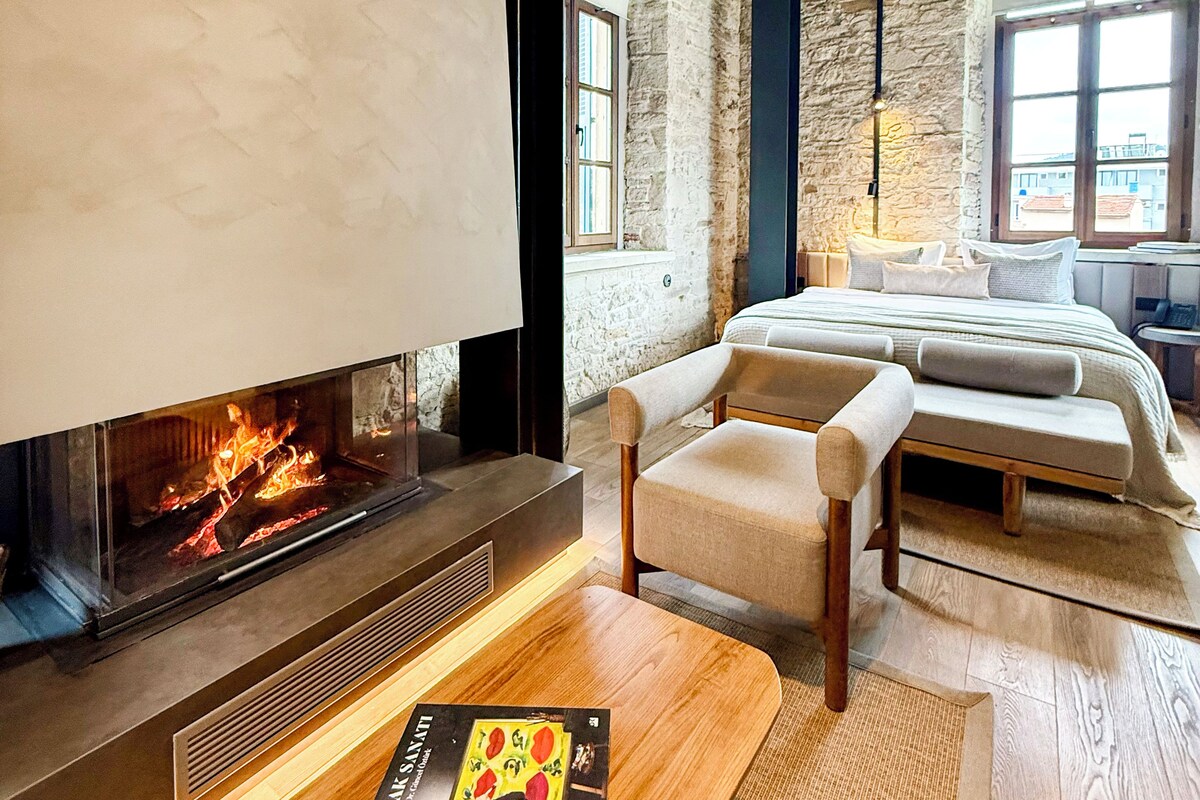 A modern living room with a fireplace, a ceiling fan, and a large window.