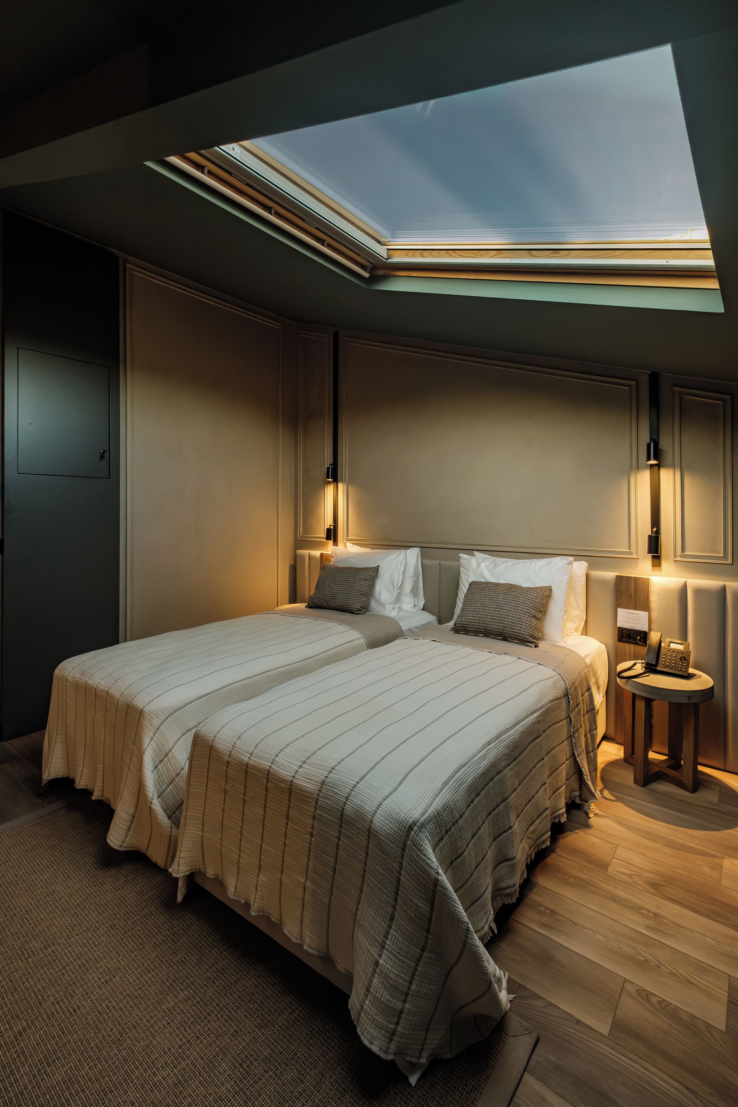 Una habitación de hotel moderna con una cama grande, un tragaluz y una mesita de noche con lámpara.