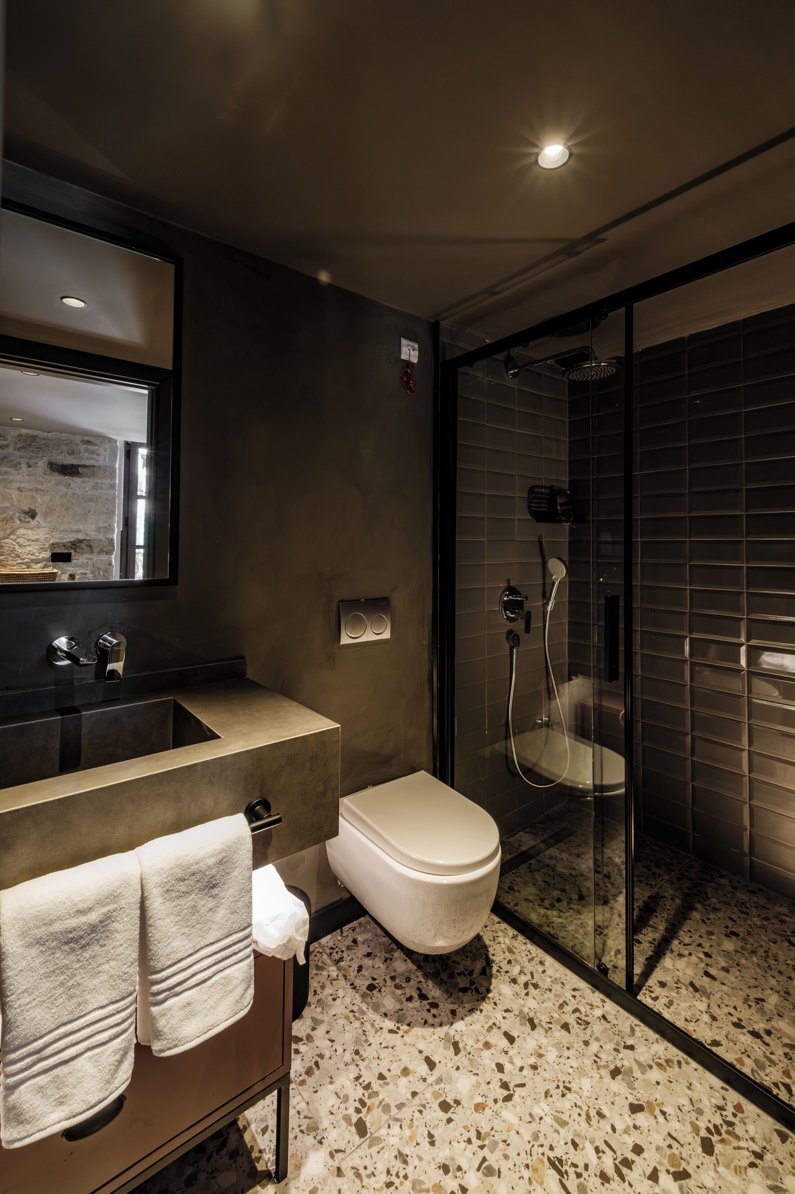 Een moderne badkamer met een douche met glazen wand, een wastafel met spiegel en een toilet.