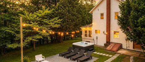 A backyard with a hot tub, outdoor seating, and string lights.