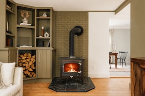 A living room with a wood-burning stove, a bookshelf, a dining area with a table and chairs, and a fireplace.