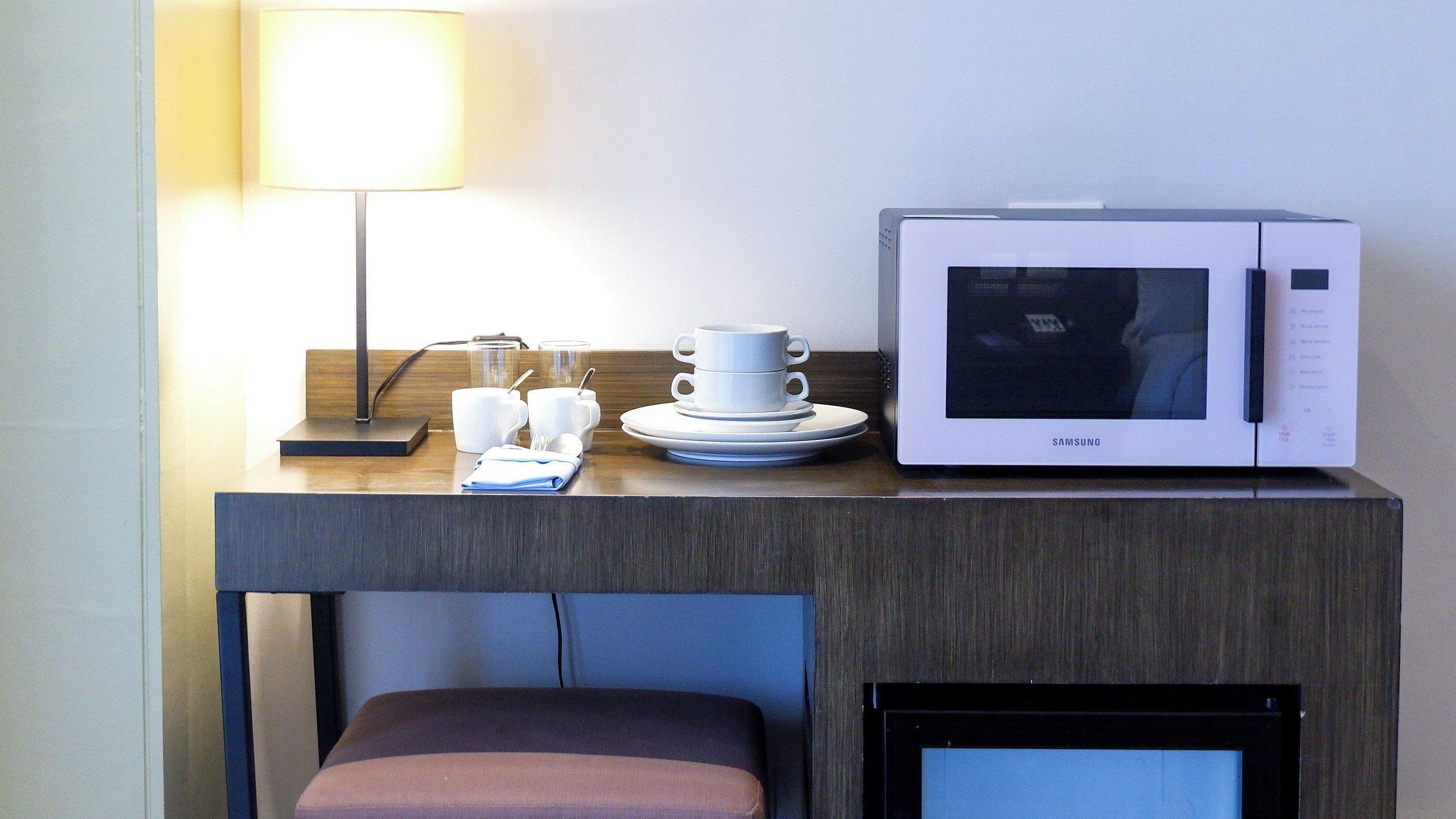Een hotelkamer met een magnetron, een lamp en een klein tafeltje met kopjes en borden.