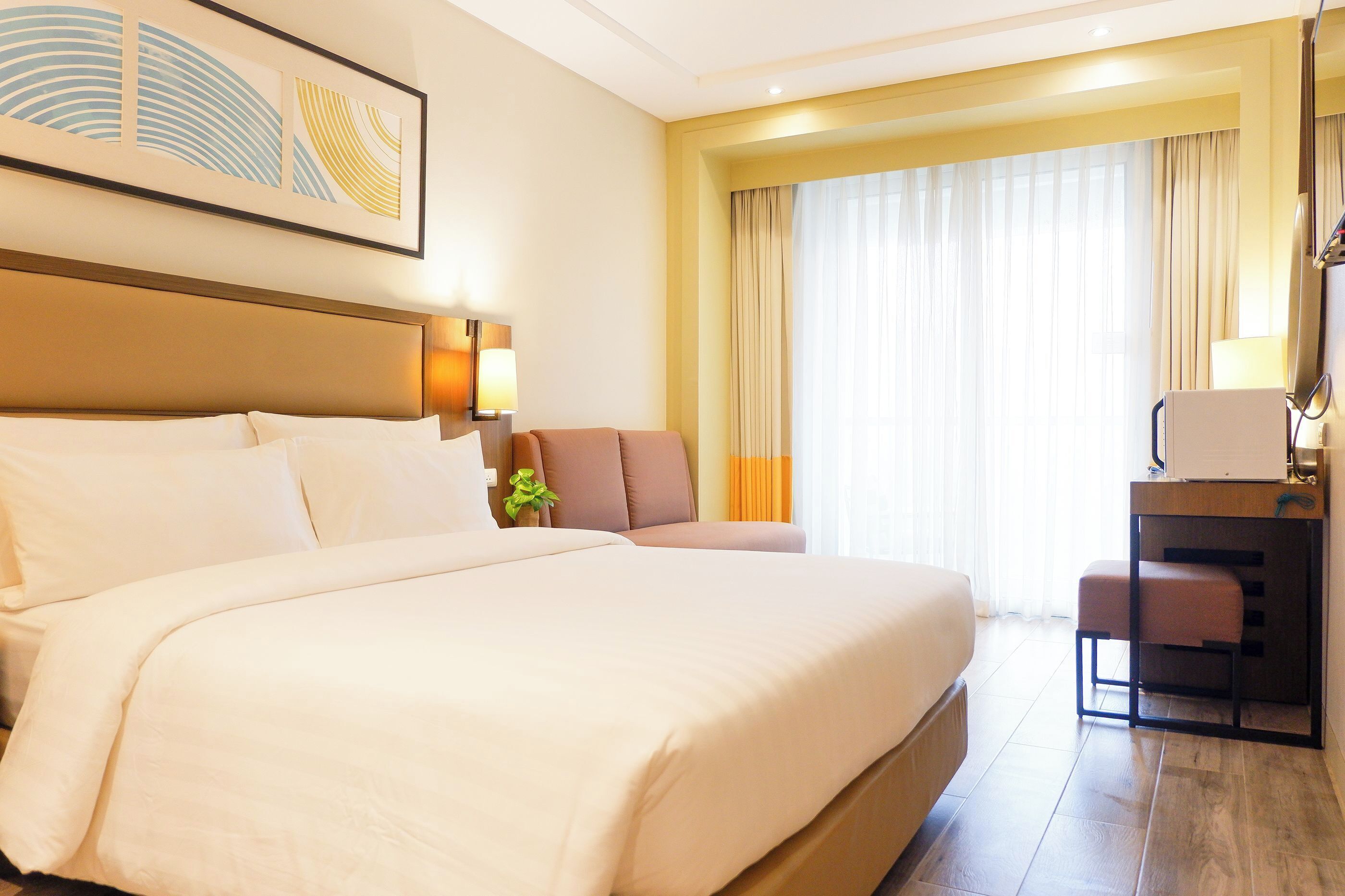 Une chambre d’hôtel avec un grand lit, un bureau avec une chaise, une petite table et une fenêtre avec des rideaux.