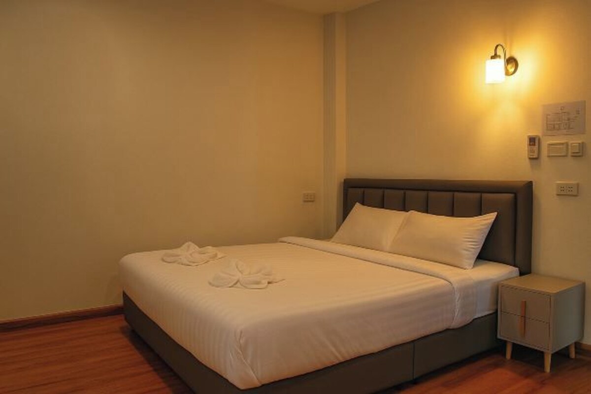 A neatly made bed with white linens and a headboard, a bedside table with a drawer, and a wall-mounted light fixture.