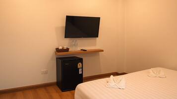 Habitación de hotel con una cama, un televisor de pantalla plana montado en la pared, un refrigerador pequeño y un estante de madera con artículos de aseo.