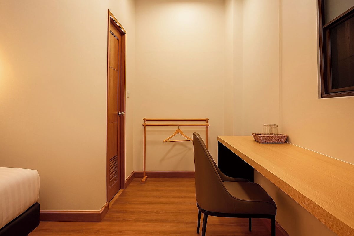 Een kleine, netjes ingerichte kamer met een bed, een houten bureau, een stoel en een kledingrek.