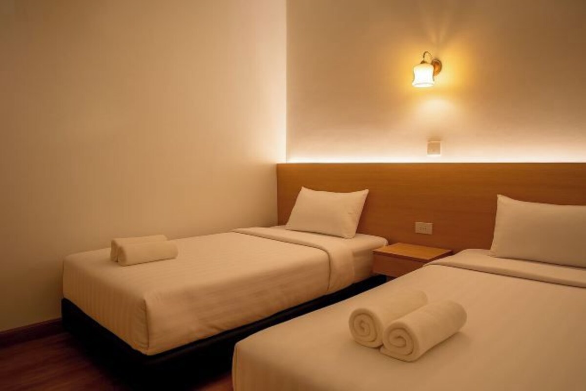 A hotel room with two beds, each with a rolled towel and a nightstand.