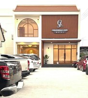 Un hotel con fachada moderna, un logotipo destacado y un estacionamiento con varios automóviles.