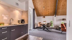 Una cocina moderna con un ventanal grande, un comedor con mesa y sillas, y un techo con vigas de madera a la vista.