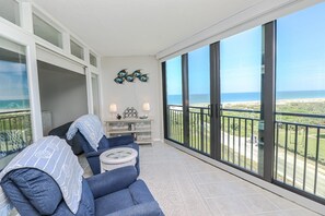 Een balkon met uitzicht op de oceaan, een blauwe bank, een tafeltje en decoratieve wandkunst.