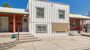 Un edificio a due piani con facciata bianca e porta rossa. Si raggiungono i vani di ingresso tramite dei gradini, e c’è un piccolo portico con una sedia e un tavolo.