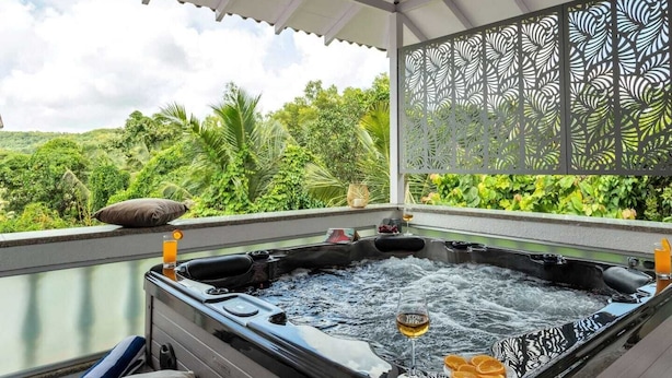 Ein Whirlpool mit einem Weinglas und Orangen, umgeben von üppiger Vegetation und einem dekorativen Sichtschutz.