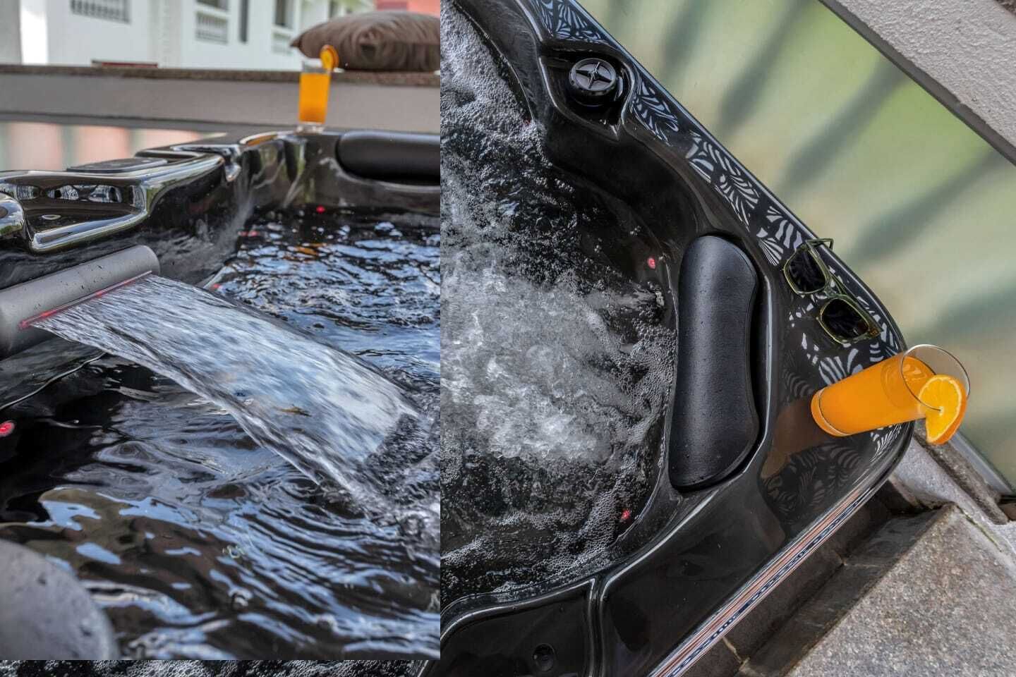 A hot tub with water flowing into it and a glass of orange juice on the side.
