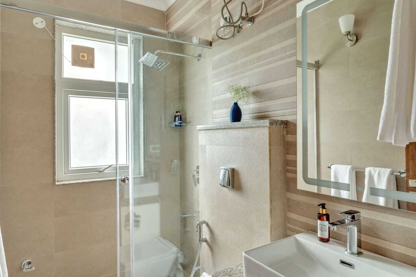 A modern bathroom with a glass shower enclosure, a large mirror, and a vanity with a sink and towel rack.