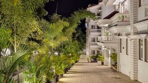 Nachtsicht eines Hotelkorridors mit Pflasterweg, Kübelpflanzen und weißen Gebäuden mit Balkonen.