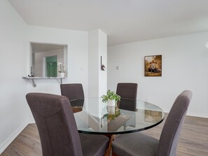 Un comedor moderno con una mesa de vidrio rodeada por cuatro sillas, una planta en maceta y un cuadro en la pared.