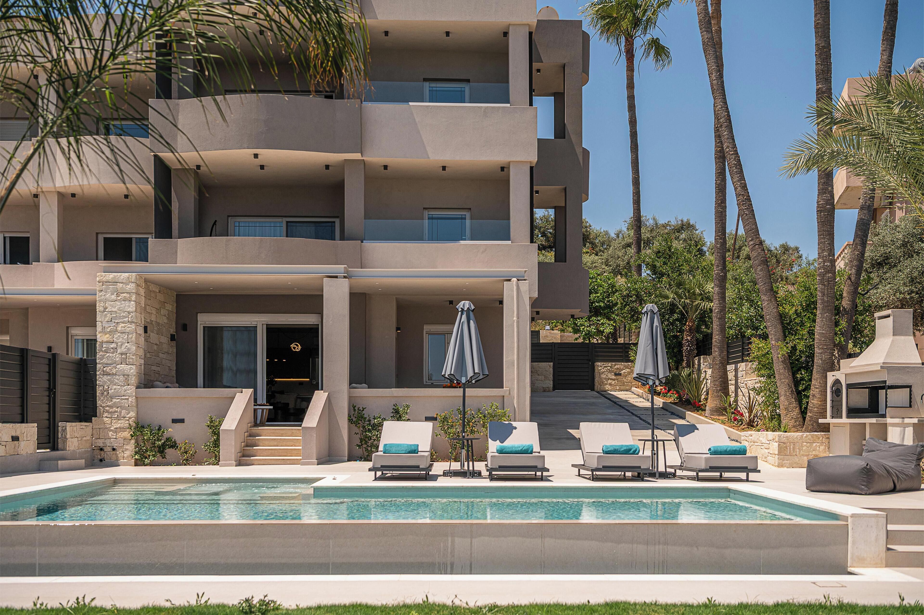 Un edificio moderno de varios pisos con piscina, mobiliario exterior y palmeras.